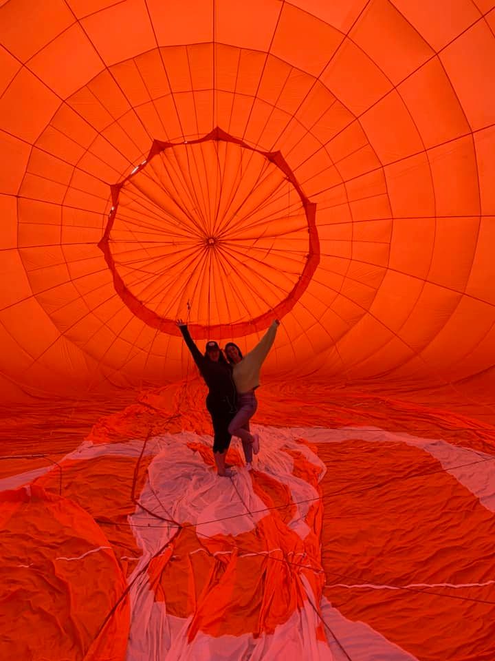 Passengers in a hot air balloon basket smiling over green fields